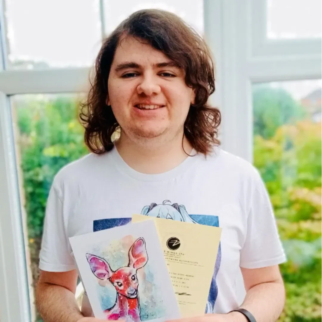 An image of Leigham W, a customer, enjoying her free print of a watercolour female deer portrait . He is smiling in his conservatory, holding up the small hand signed and numbered watercolour print and the certificate of authenticity from Jamie C. Goodwin available at JamieHasWings.com