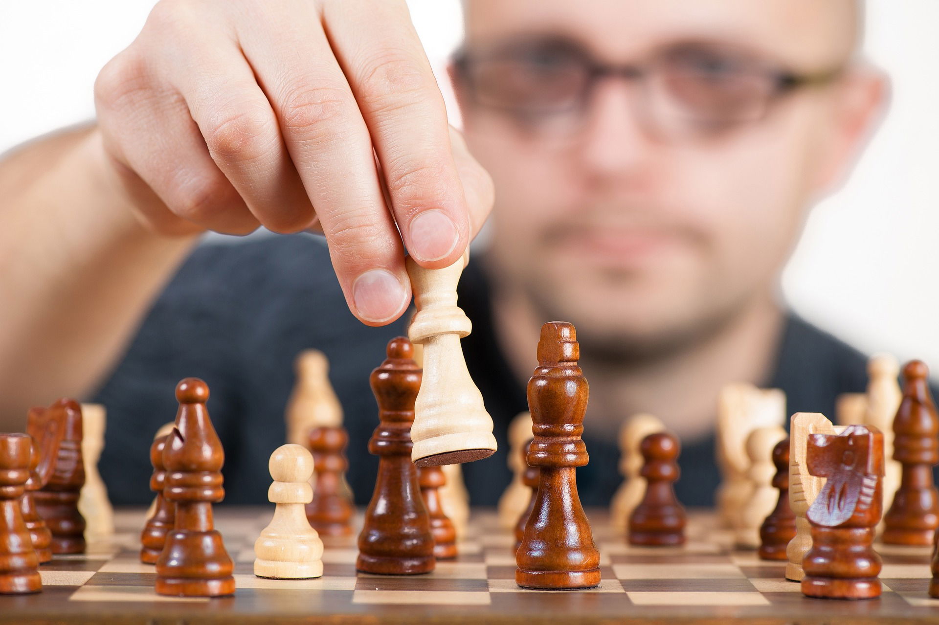 Close-up of a hand moving a chess piece, symbolizing strategic decision-making. The player, a man in glasses, focuses intently, reflecting the careful planning and precision involved in building successful Christian websites and marketing strategies.