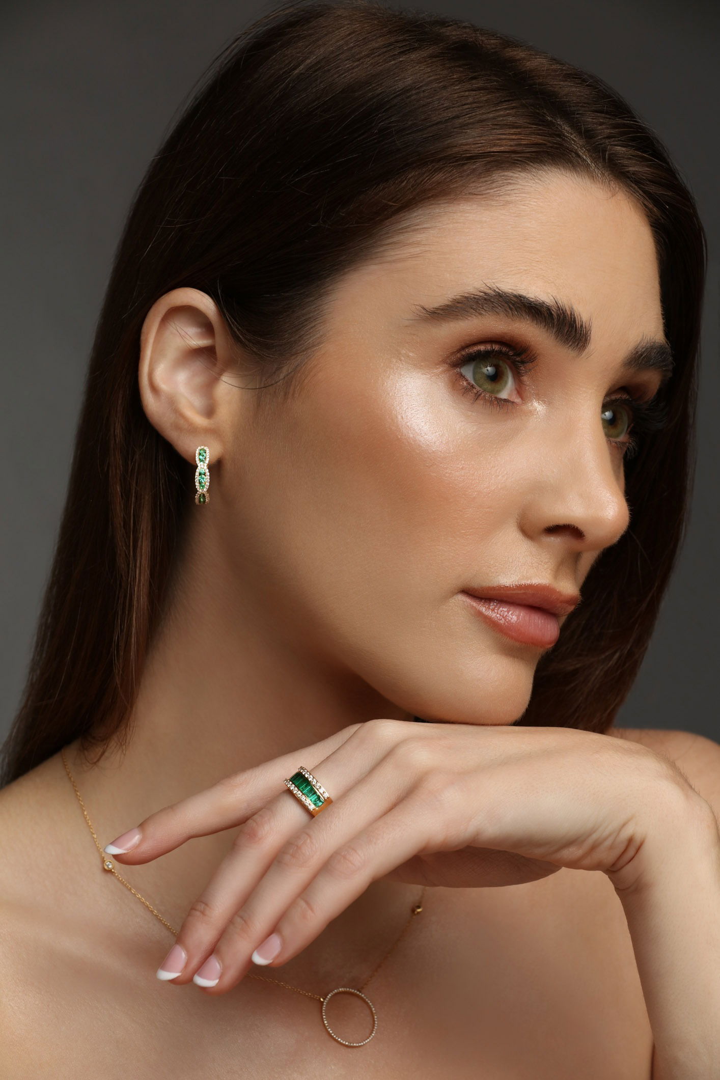 Close-up studio image of green gemstone ring and earring worn together on model