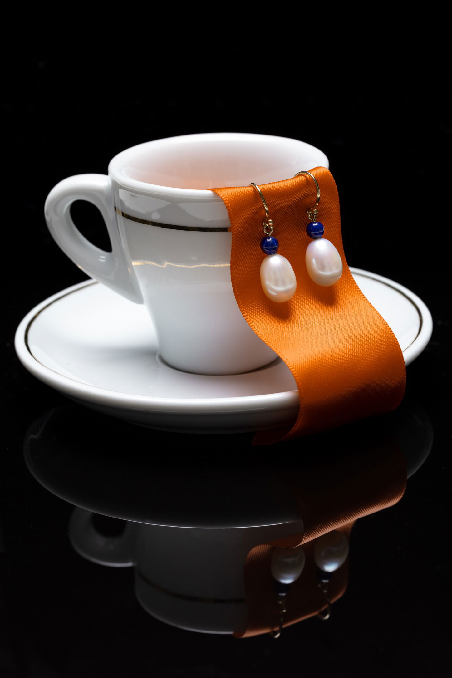 pearl earrings hanging off a teacup with an orange ribbon