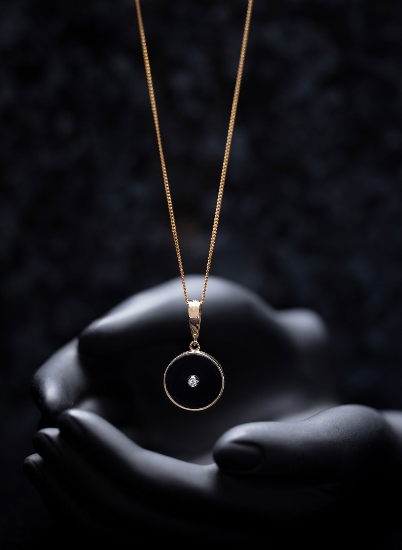 Dainty black and gold necklace dangling over black hand sculpture
